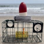 Crab pot buoy sitting on top of a crab trap on a beach.