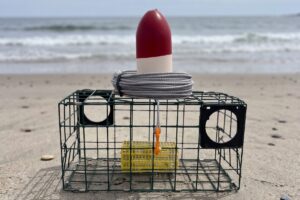 Crab pot buoy sitting on top of a crab trap on a beach.